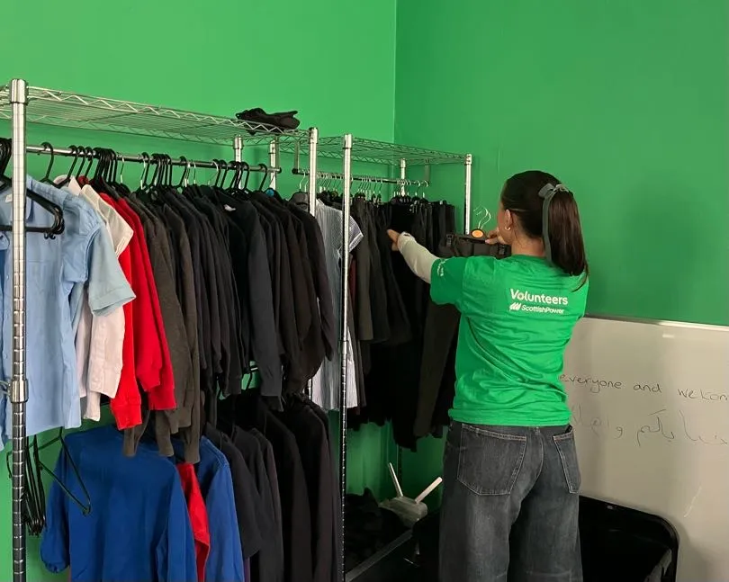Woman in green Scottish Power volunteers t-shirt stacking clothing rails